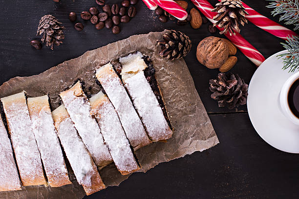 Advent Slice of fresh baked homemade strudel with poppy seeds and sugar powder, on a black background and fir branches. Cocoa with murshmelou. Christmas, winter still life